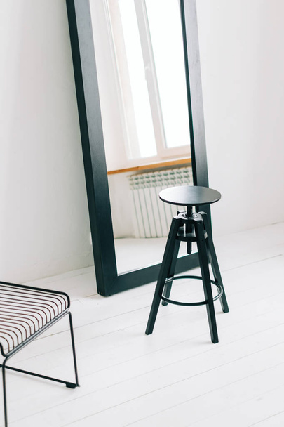 Big black mirror with black wooden chair in bright room near window. - Foto, afbeelding