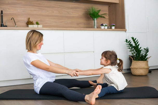 Woman and her little daughter are stretching while practicing together at home - Fotografie, Obrázek