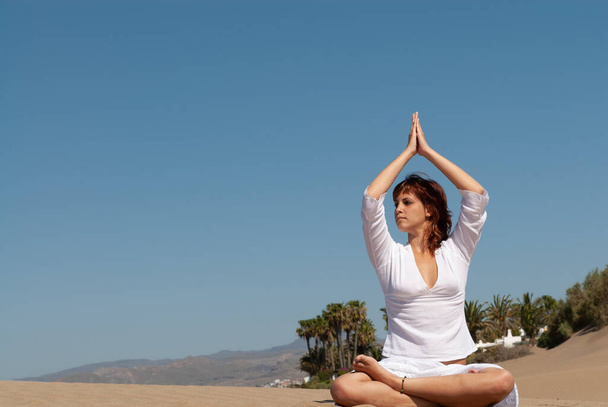 woman doing meditation poses on sand dunes under blue sky - Zdjęcie, obraz