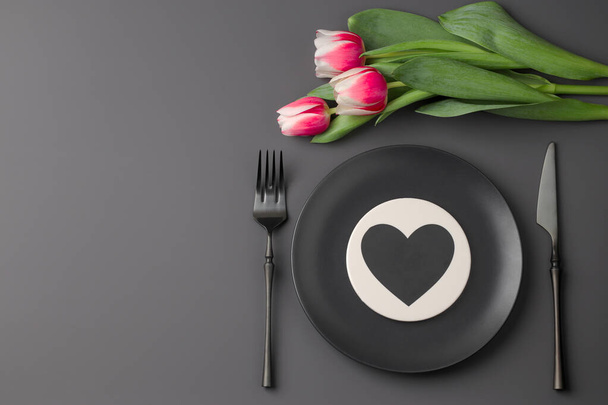 Festive creative black table setting with heart and tulip bouquet on dark background. Valentine's Day, Wedding Day, Birthday, Women's Day and Mother's Day. Flat lay. Copy space - Фото, изображение
