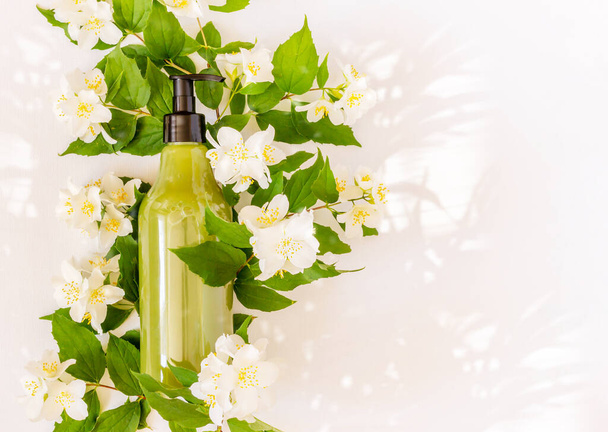 Bottle for branding and label on a blooming Jasmin branch with sun glare - Foto, afbeelding
