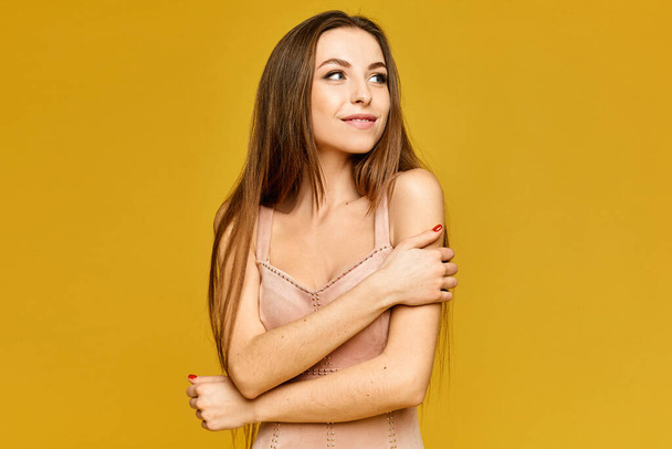 Young woman with gentle makeup in a beige dress on the yellow background. Model girl in elegant outfit isolated on the yellow background - Foto, imagen