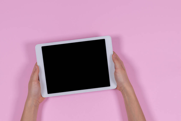 Manos sosteniendo la tableta digital sobre fondo rosa pastel - Foto, Imagen