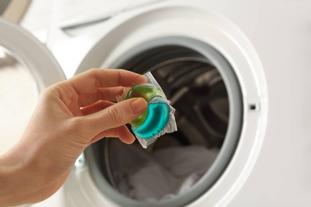 Woman holding laundry detergent capsule near washing machine, closeup - Photo, image