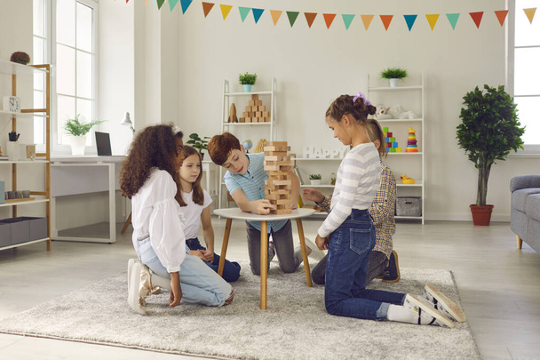 Group of quiet kids playing wood block tower stacking game at home or in leisure club - Photo, Image