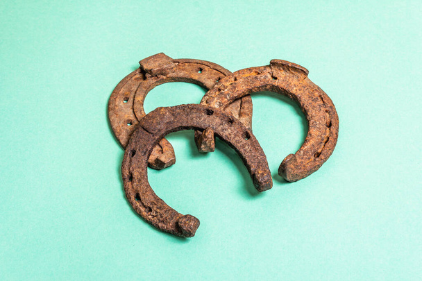 Cast iron metal horseshoes. Good luck symbol, festive concept. Badly worn rusty horse accessories, matte turquoise background, place for text - Photo, Image