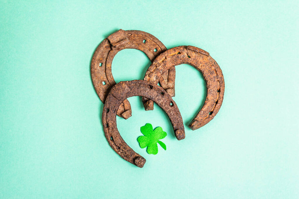 Badly worn horseshoes with a felt clover leaf. Good luck symbol, St.Patrick's day concept. Matte turquoise background, top view - Photo, Image