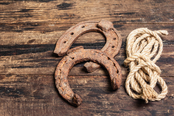Cast iron metal horseshoes and rope. Good luck symbol, badly worn rusty horse accessories. Vintage wooden boards background - Fotoğraf, Görsel
