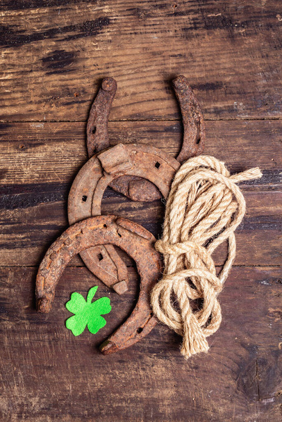Badly worn horseshoes, rope, and felt clover leaf. Good luck symbol, St.Patrick's day concept. Vintage wooden boards background - Photo, Image