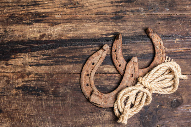 Cast iron metal horseshoes and rope. Good luck symbol, badly worn rusty horse accessories. Vintage wooden boards background, top view - Photo, Image