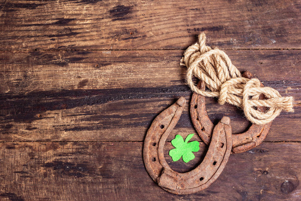 Badly worn horseshoes, rope, and felt clover leaf. Good luck symbol, St.Patrick's day concept. Vintage wooden boards background - Photo, Image