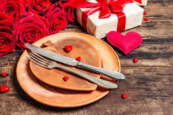 Romantický jídelní stůl. Milostný koncept na Valentýna nebo na Den matek, svatební příbory. Kytice z čerstvých burgundských růží, vinobraní dřevěné desky na pozadí - Fotografie, Obrázek