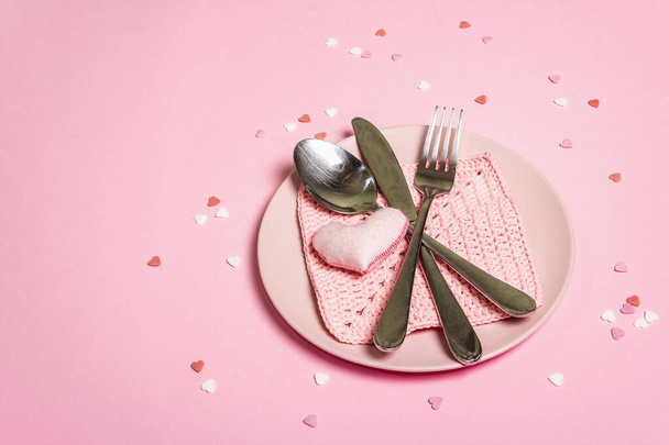 Romantic dinner table. Love concept for Valentine's or mother's day, wedding cutlery. Minimalistic style, rose plates, crochet napkin, scattered pastry topping, place for text - Photo, Image