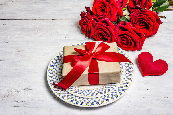 Romantický jídelní stůl. Milostný koncept na Valentýna nebo na Den matek, svatební příbory. Kytice z čerstvých burgundských růží, slavnostní dárek, starý dřevěný stůl - Fotografie, Obrázek
