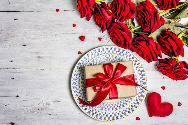 Romanttinen ruokapöytä. Rakkaus käsite Ystävänpäivä tai äitienpäivä, häät ruokailuvälineet. Kukkakimppu tuoreita viininpunainen ruusuja, juhlava lahja, vanha puinen pöytä - Valokuva, kuva