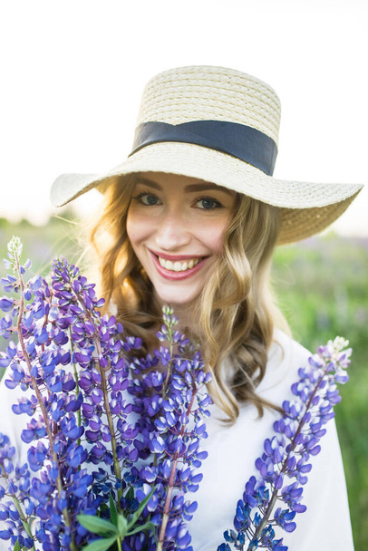 a young beautiful girl in a white dress and hat walks across the field with lupins - Foto, immagini