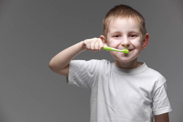 Niño niño feliz niño cepillarse los dientes con cepillo de dientes sobre fondo gris. Salud, higiene dental. Mockup, espacio de copia. - Foto, imagen