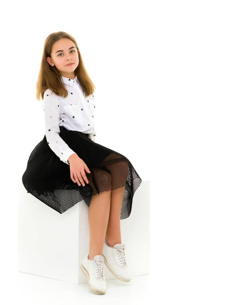 Portrait of a cute girl sitting on a white cube hands on her knees - Foto, imagen