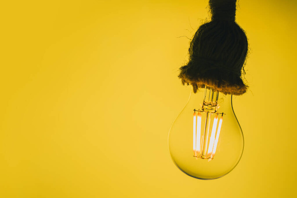 Close-up weergave van een transparante LED-lamp die lijkt op een oude wolfraam lamp op een gele achtergrond en pluizig stopcontact. - Foto, afbeelding