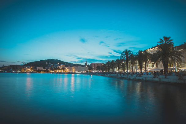 Split in croata 'nın mavi saatinde akşam manzarası, gün batımından hemen sonra gezinti güvertesinde veya rivada görünen palmiyeler ve turistler. Güzel bölünmüş şehir manzarası - Fotoğraf, Görsel
