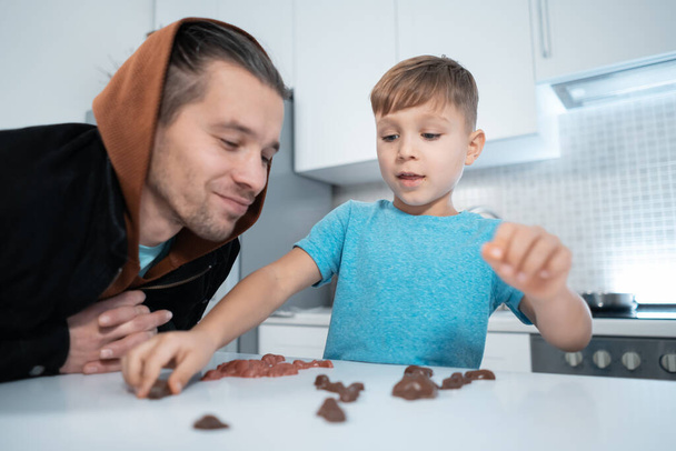 happy father and kid boy play with chocolate sweets and have fun at home kitchen - Zdjęcie, obraz
