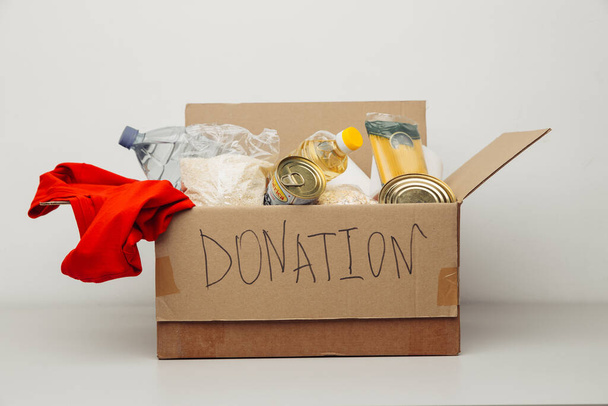 Caja de donaciones. Caja de cartón abierta con ropa y comida sobre fondo blanco. Concepto de caridad - Foto, imagen
