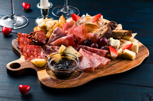 Cutting board with prosciutto, salami, cheese on dark background. wooden board with antipasto set of meat, salami and cheese for festive table - Fotografie, Obrázek