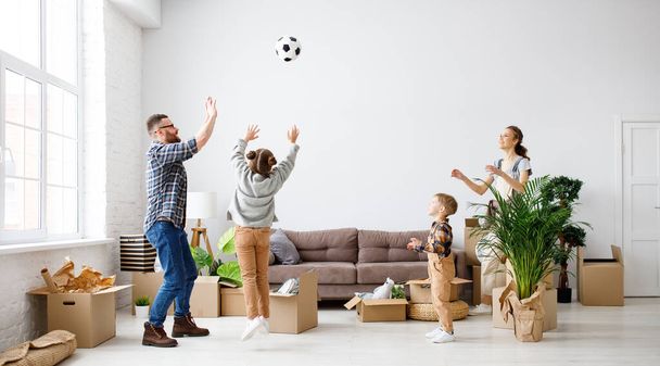Szczęśliwi rodzice i dzieci bawią się piłką nożną w nowym przestronnym mieszkaniu, ciesząc się przeprowadzką i zabawą - Zdjęcie, obraz