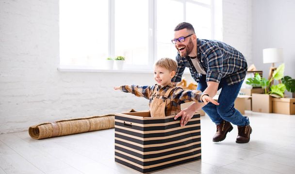 Seitenansicht des entzückten Vaters, der lächelndes Kind in Schachtel reitet und dabei Spaß beim Umzug in neue Wohnung hat - Foto, Bild