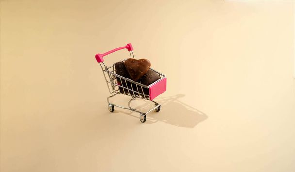 Hart em forma de chocolate em um carrinho de compras rosa bonito contra arenoso - Foto, Imagem