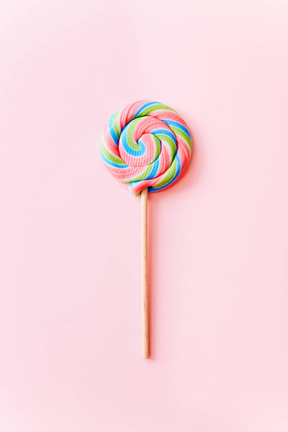 Colorful lollipop swirl on stick. Striped spiral multicolored candy on pink background, top view - Φωτογραφία, εικόνα