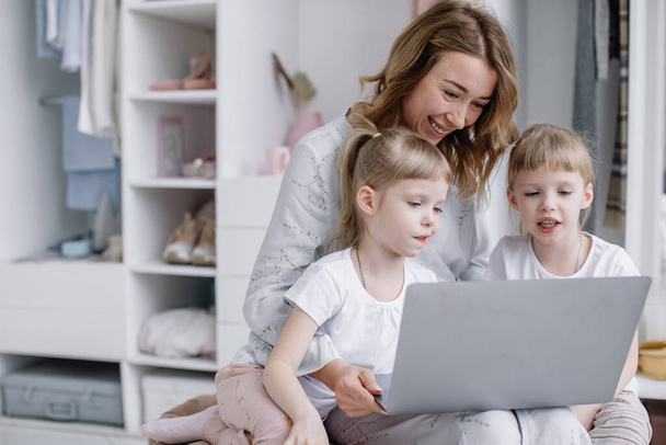 Giovane madre con le sue figlie gemelle scegliere le cose online nel suo accogliente appartamento - Foto, immagini
