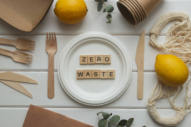 Zero waste concept. Eco-friendly disposable organic utensil. Knives, forks, plate, string bag and paper bag and inscription zero waste from wooden letters. Ecology concept. Top view, flat lay - Foto, afbeelding