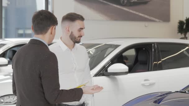 Όμορφος επιχειρηματίας μιλάει με τον πωλητή στην αντιπροσωπεία αυτοκινήτων - Πλάνα, βίντεο