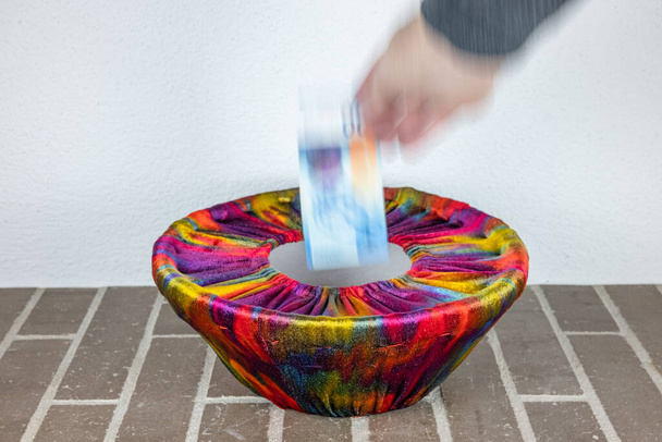 Uma mão humana deixa cair uma nota de suíço em uma cesta vestida com tecido colorido - Foto, Imagem