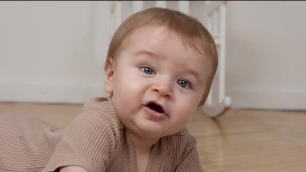 Ευτυχισμένο βρέφος. Κοντινό πλάνο του χαριτωμένου μωρού γέλιο, που βρίσκεται στο πάτωμα στο σπίτι, αργή κίνηση - Πλάνα, βίντεο