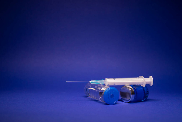 zwei transparente Vaccine Flasche ohne Etikett, medizinische Spritze Injektionsnadel. isoliert auf blauem Hintergrund. Entwicklung eines Coronavirus-Impfstoffs COVID-19. Weltrennen in der Forschung. Kopierraum - Foto, Bild