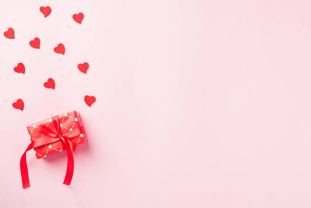 Valentines' day background. Red gift box with ribbon bow and wood red hearts shaped composition greeting card for love isolated on pink background with copy space. Top View from above - Φωτογραφία, εικόνα