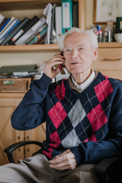 Telefonda konuşan yaşlı bir adam evde oturuyor. - Fotoğraf, Görsel