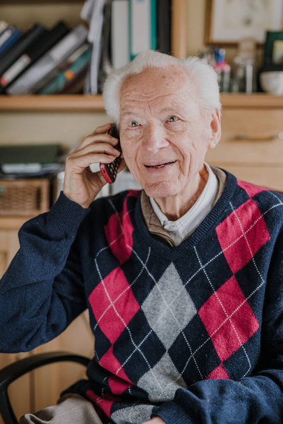 Homme âgé parlant au téléphone assis à la maison - Photo, image