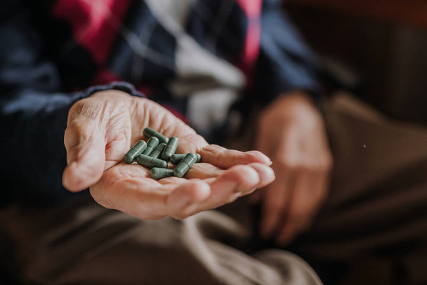 Старий тримає жменьку зелених таблеток в руці
 - Фото, зображення