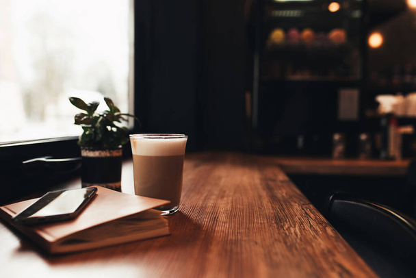 Cup of coffee, notebook, phone at table in cafe. Blurred background - Фото, зображення