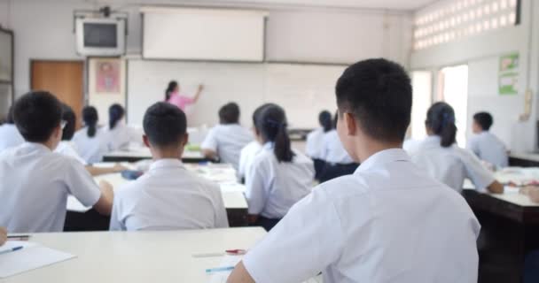 Zeitlupe asiatischer High-School-Schüler in weißer Uniform, die aktiv ihre Hände heben, um Fragen auf einer Projektionswand zu beantworten, die ihnen Lehrer im Klassenzimmer stellen. - Filmmaterial, Video