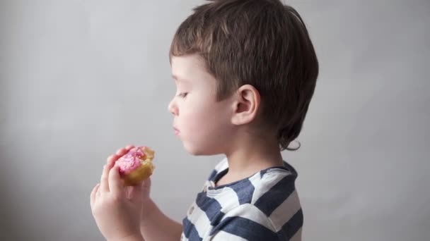 Kis fehér fiú rózsaszín fánkot eszik. Jó étvágyat. Közelről.. - Felvétel, videó