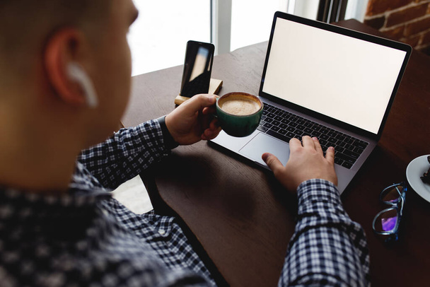 Man working at laptop with cup of coffee, headphones at home. Blurred background - Photo, Image
