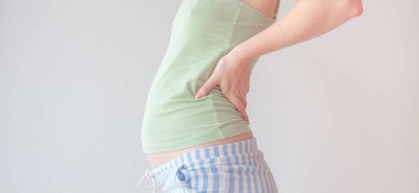 Mulher grávida segura a parte inferior das costas, sofre de dor lombar. A gestante sofre de dor nas costas no segundo trimestre de gravidez. Tratamento e prevenção - Foto, Imagem