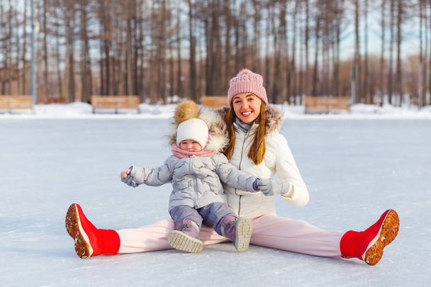 Happy young woman and one-and-a-half-year-old girl in winter in warm jackets walk in the park. mother and daughter in winter clothes. - Photo, image