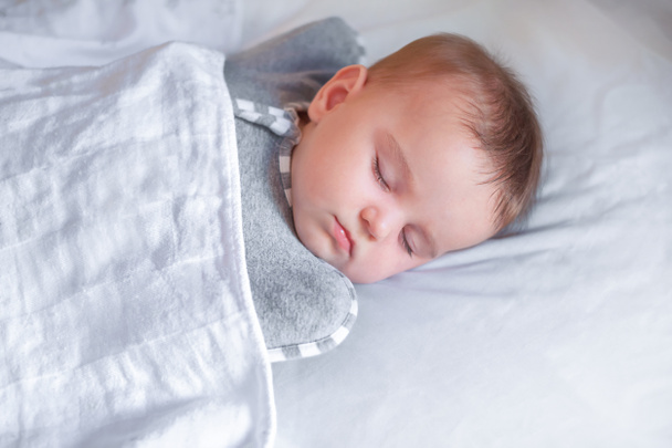 Cute baby sleeps in the crib. The child sleeps sweetly on a white sheet - Фото, изображение