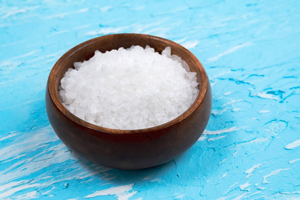 White sea salt in a natural wooden bowl blue background. Selective focus. copyspace - Photo, Image