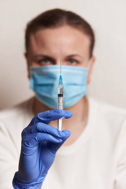 a woman holds an injection syringe in front of her. Vaccination in a pandemic - Photo, image